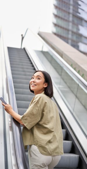 young-happy-woman-standing-escalator-with-smartphone-going-up-walking-city